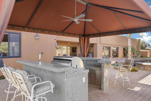 view of patio with exterior kitchen, ceiling fan, a bar, and grilling area