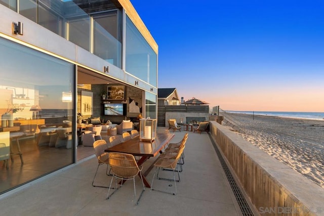 patio terrace at dusk featuring a water view and a beach view