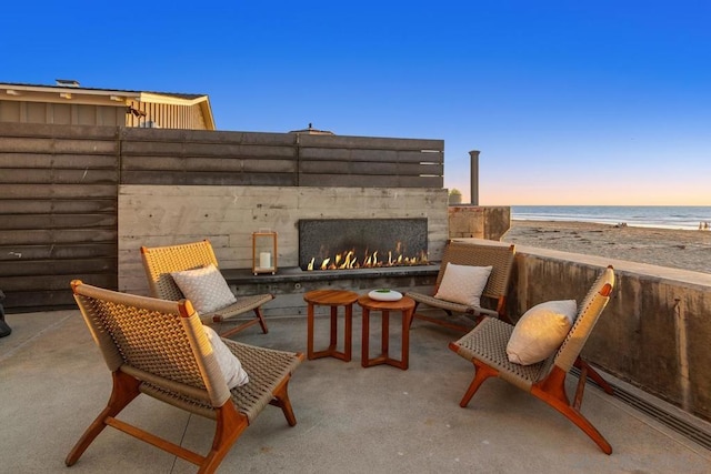 patio terrace at dusk featuring a water view and a view of the beach