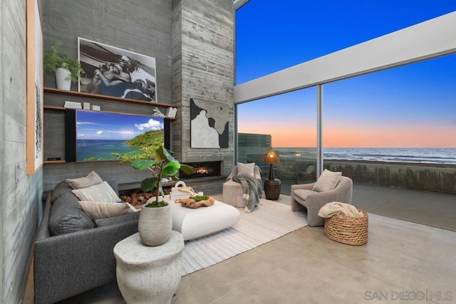 living room with a view of the beach, concrete flooring, a large fireplace, and a water view