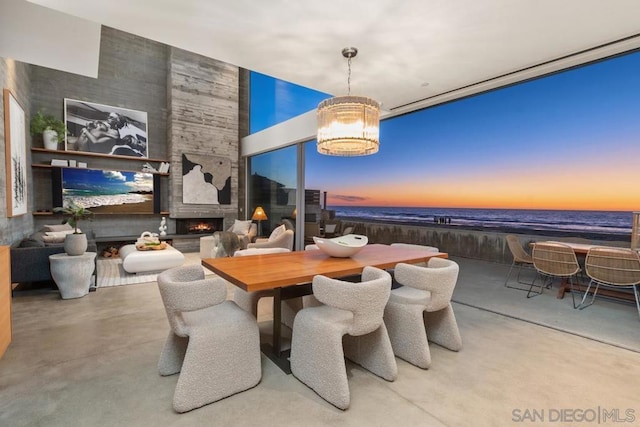 dining room featuring a view of the beach, a water view, concrete flooring, an inviting chandelier, and a fireplace