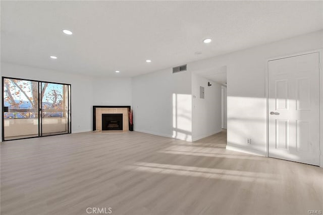 unfurnished living room with a tiled fireplace and light wood-type flooring