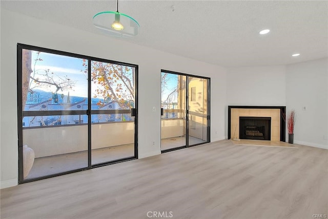 unfurnished living room with a tiled fireplace, a healthy amount of sunlight, and light hardwood / wood-style flooring