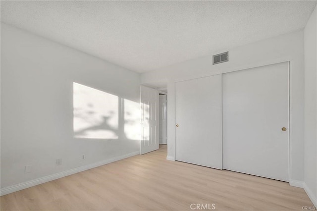 unfurnished bedroom featuring light hardwood / wood-style flooring, a textured ceiling, and a closet