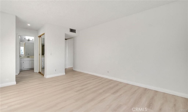 unfurnished bedroom with connected bathroom, a textured ceiling, and light wood-type flooring