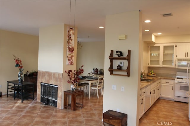 kitchen with white appliances, sink, light tile patterned floors, a fireplace, and white cabinetry