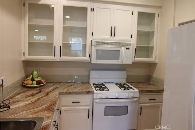 kitchen with light stone countertops, sink, white cabinets, and white appliances