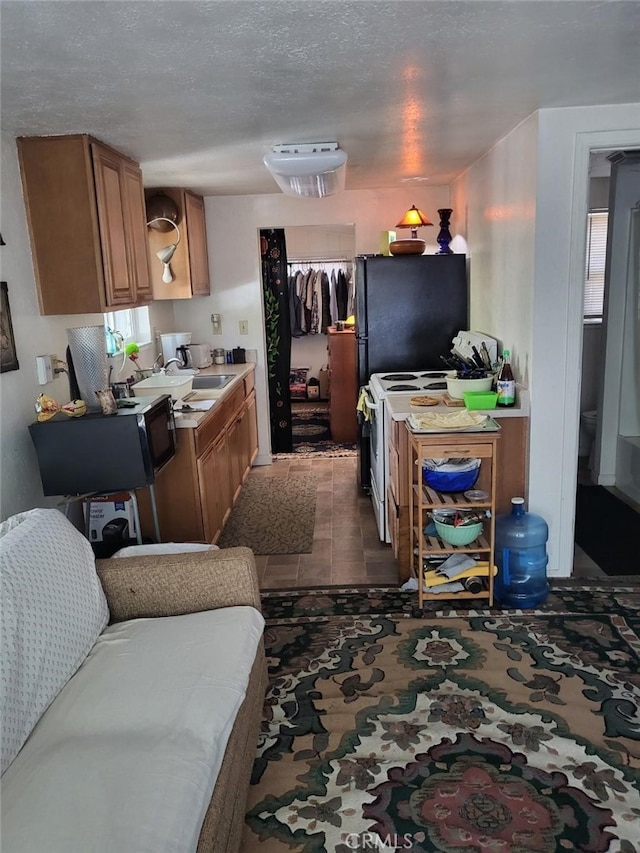 kitchen featuring black fridge, a textured ceiling, white range with electric stovetop, dark tile patterned floors, and sink