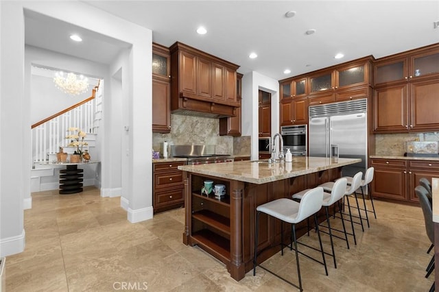 kitchen with light stone counters, stainless steel appliances, a sink, a kitchen breakfast bar, and a center island with sink