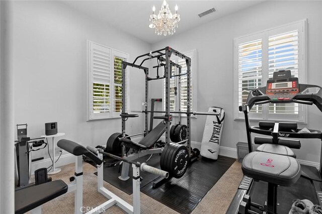 exercise room featuring an inviting chandelier, visible vents, and baseboards
