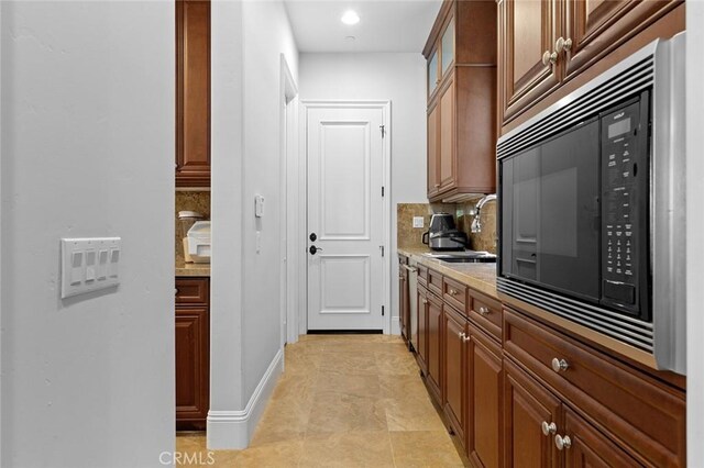 kitchen with black microwave, light stone counters, a sink, backsplash, and glass insert cabinets