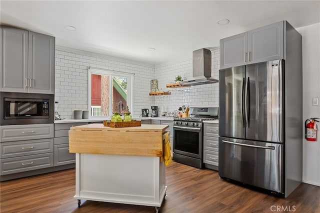 kitchen with appliances with stainless steel finishes, dark wood-type flooring, wall chimney range hood, and gray cabinetry