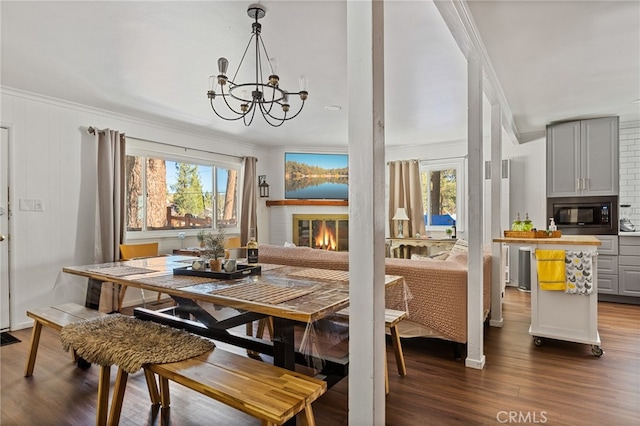 dining space with wood-type flooring, ornamental molding, a fireplace, and an inviting chandelier