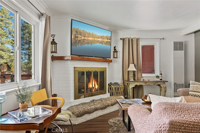 living area with wood-type flooring, ornamental molding, and a brick fireplace