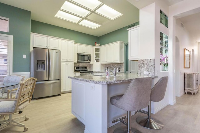 kitchen with stainless steel appliances, light stone countertops, kitchen peninsula, a kitchen bar, and white cabinets