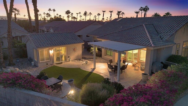 back house at dusk featuring a yard and a patio area