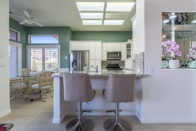 kitchen with stainless steel appliances, light stone countertops, kitchen peninsula, white cabinetry, and tasteful backsplash