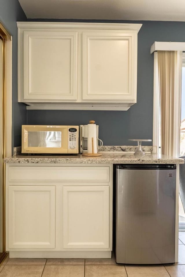 kitchen featuring light tile patterned floors, white cabinetry, stainless steel refrigerator, and a wealth of natural light