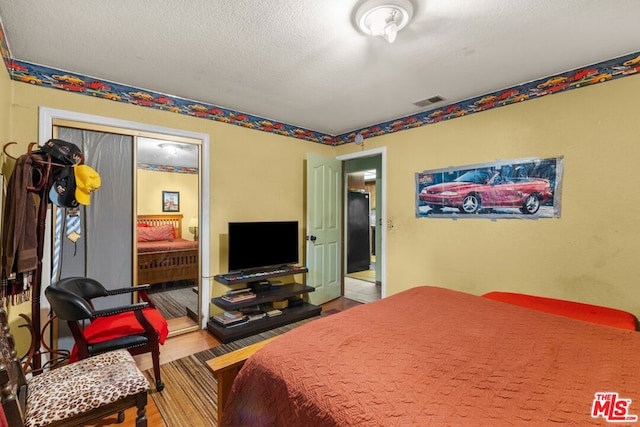 bedroom featuring hardwood / wood-style floors, black fridge, a textured ceiling, and a closet