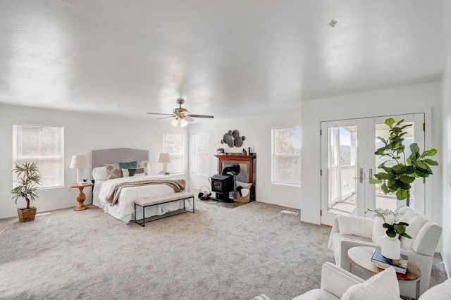 bedroom with ceiling fan, a wood stove, access to outside, light colored carpet, and french doors