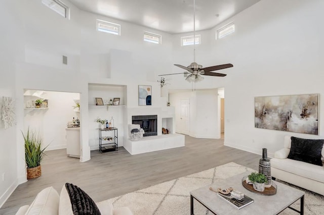 living room with ceiling fan, a towering ceiling, and light hardwood / wood-style floors