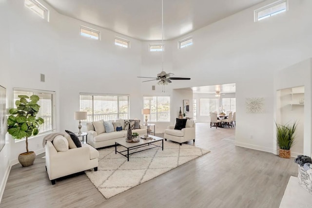 living room with ceiling fan, a towering ceiling, and light hardwood / wood-style floors