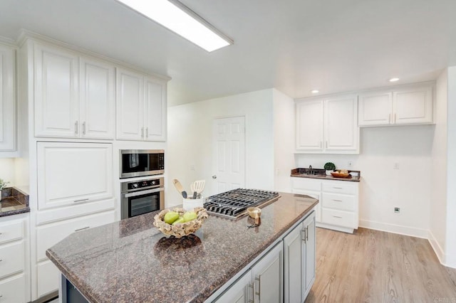 kitchen featuring a kitchen island, light hardwood / wood-style flooring, appliances with stainless steel finishes, white cabinets, and dark stone counters