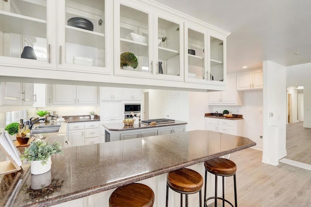 kitchen with stainless steel microwave, light hardwood / wood-style floors, a center island, sink, and white cabinets