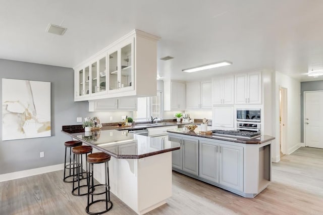 kitchen with appliances with stainless steel finishes, white cabinetry, light hardwood / wood-style floors, sink, and kitchen peninsula