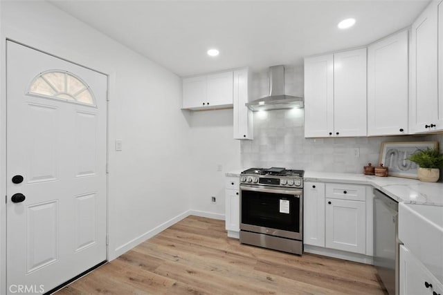 kitchen featuring wall chimney range hood, backsplash, light hardwood / wood-style floors, white cabinets, and appliances with stainless steel finishes