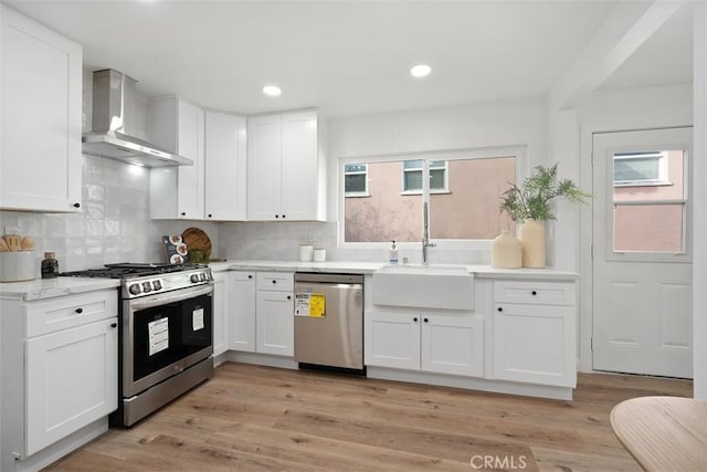 kitchen featuring white cabinets, wall chimney exhaust hood, light hardwood / wood-style floors, and stainless steel appliances