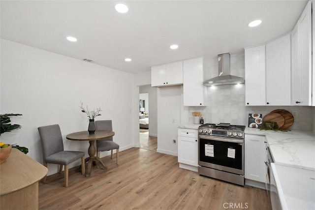 kitchen with stainless steel range with gas cooktop, wall chimney range hood, tasteful backsplash, light hardwood / wood-style floors, and white cabinetry