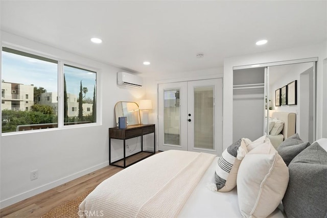 bedroom featuring a wall mounted air conditioner, light hardwood / wood-style floors, and french doors