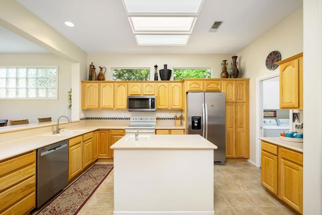 kitchen featuring sink, a center island, light brown cabinets, washer and dryer, and appliances with stainless steel finishes