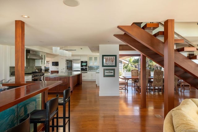 kitchen featuring hardwood / wood-style floors, tasteful backsplash, white cabinetry, stainless steel counters, and wall chimney exhaust hood