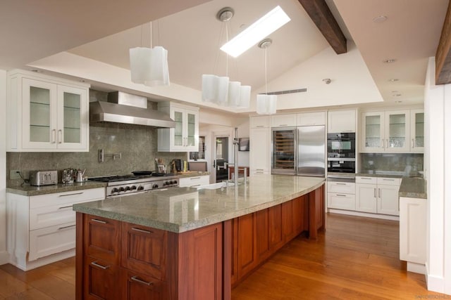 kitchen with white cabinetry, wall chimney range hood, decorative light fixtures, and a center island with sink