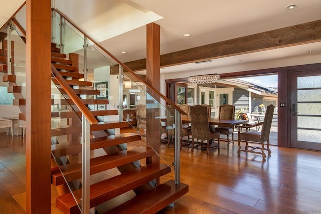 stairs featuring french doors, beam ceiling, wood-type flooring, and an inviting chandelier