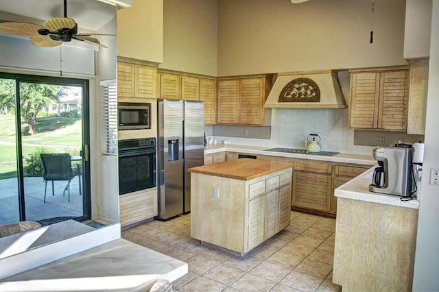 kitchen featuring premium range hood, light tile patterned floors, ceiling fan, black appliances, and a center island