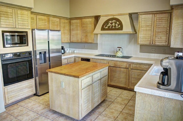 kitchen with black appliances, custom exhaust hood, light tile patterned floors, and a center island