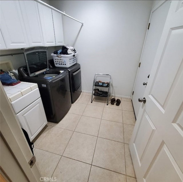 laundry area featuring washer and clothes dryer, light tile patterned flooring, and cabinets