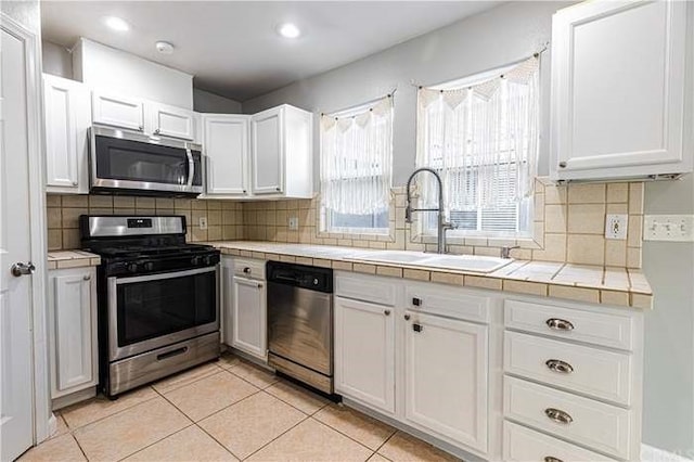 kitchen with tile countertops, white cabinets, sink, light tile patterned floors, and stainless steel appliances