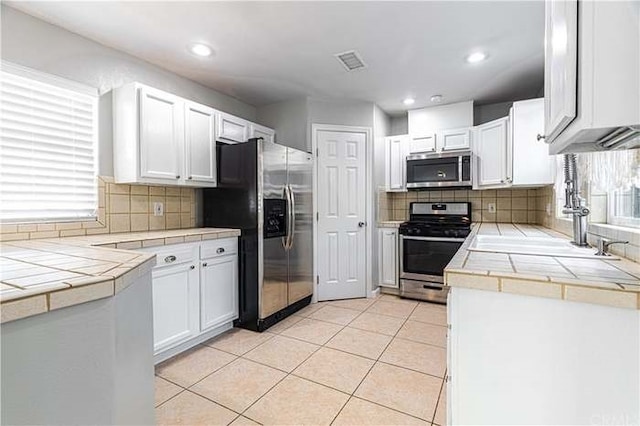 kitchen with backsplash, tile countertops, white cabinetry, and stainless steel appliances