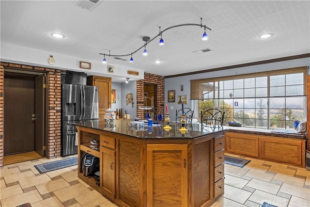 kitchen with stainless steel fridge with ice dispenser, a center island with sink, dark stone counters, and ornamental molding