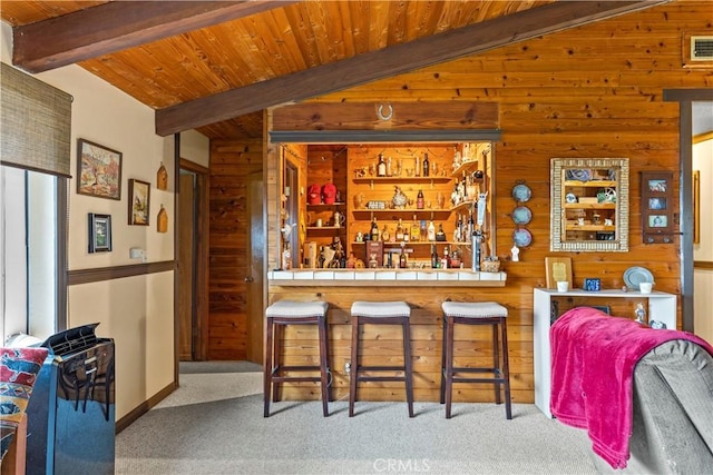 bar with vaulted ceiling with beams, light colored carpet, wooden ceiling, and wooden walls