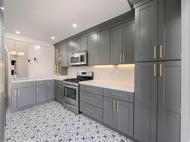 kitchen with gray cabinets, pendant lighting, tasteful backsplash, sink, and stainless steel appliances