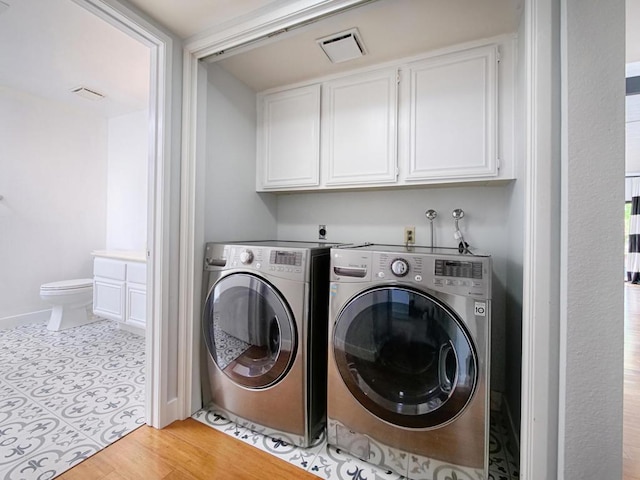 washroom with washing machine and dryer, cabinets, and light wood-type flooring