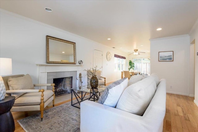 living room with ceiling fan, light wood-type flooring, crown molding, and a fireplace