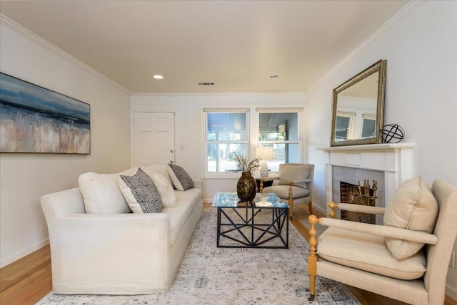 living room featuring light wood-type flooring, ornamental molding, and a tile fireplace