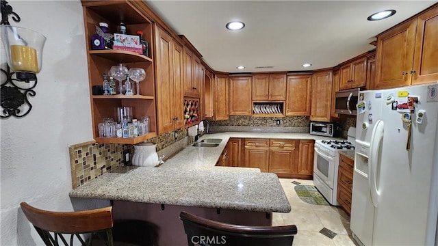 kitchen featuring backsplash, kitchen peninsula, a kitchen bar, sink, and white appliances