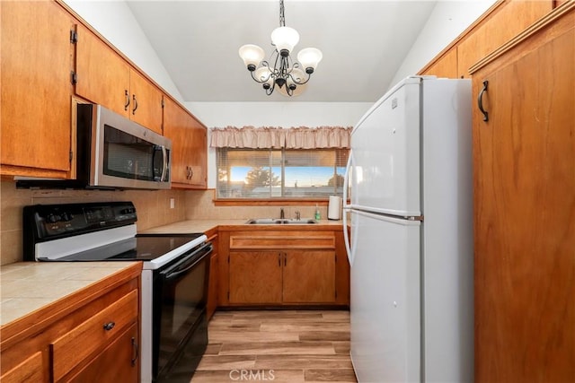 kitchen with light wood-type flooring, vaulted ceiling, an inviting chandelier, white fridge, and black / electric stove